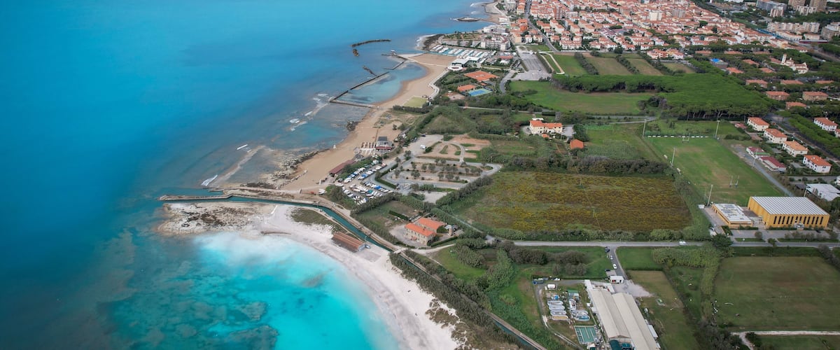 An aerial view of a coastal town with a beach, marina, and residential areas.