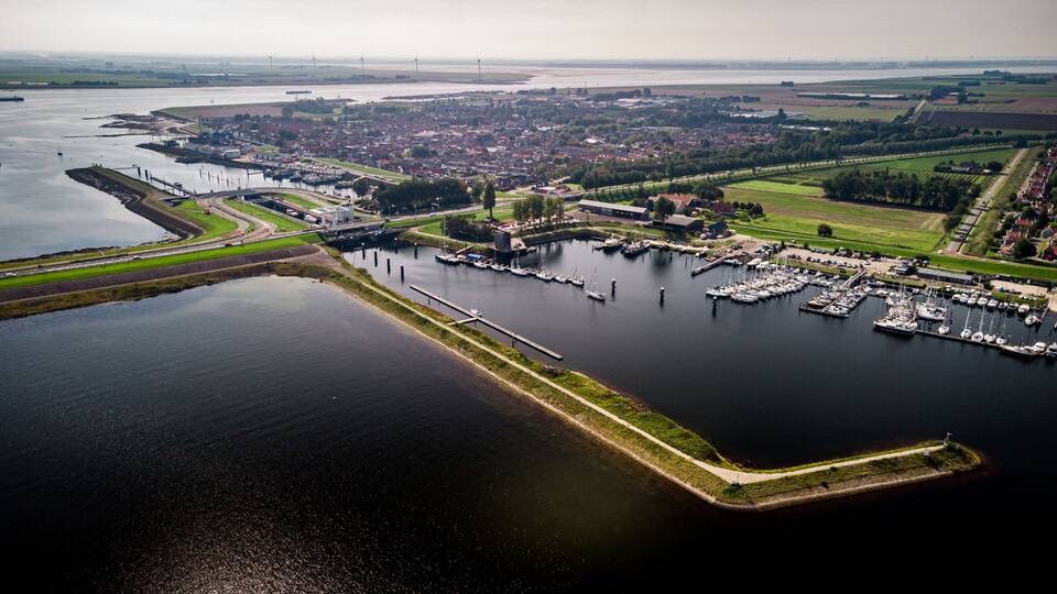 An aerial view of a marina with boats docked, a bridge crossing a river, and a town in the background.