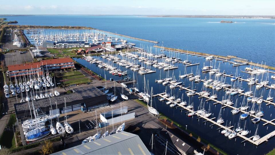 A marina with numerous boats docked, a pier extending into the water, and a building with a red roof.