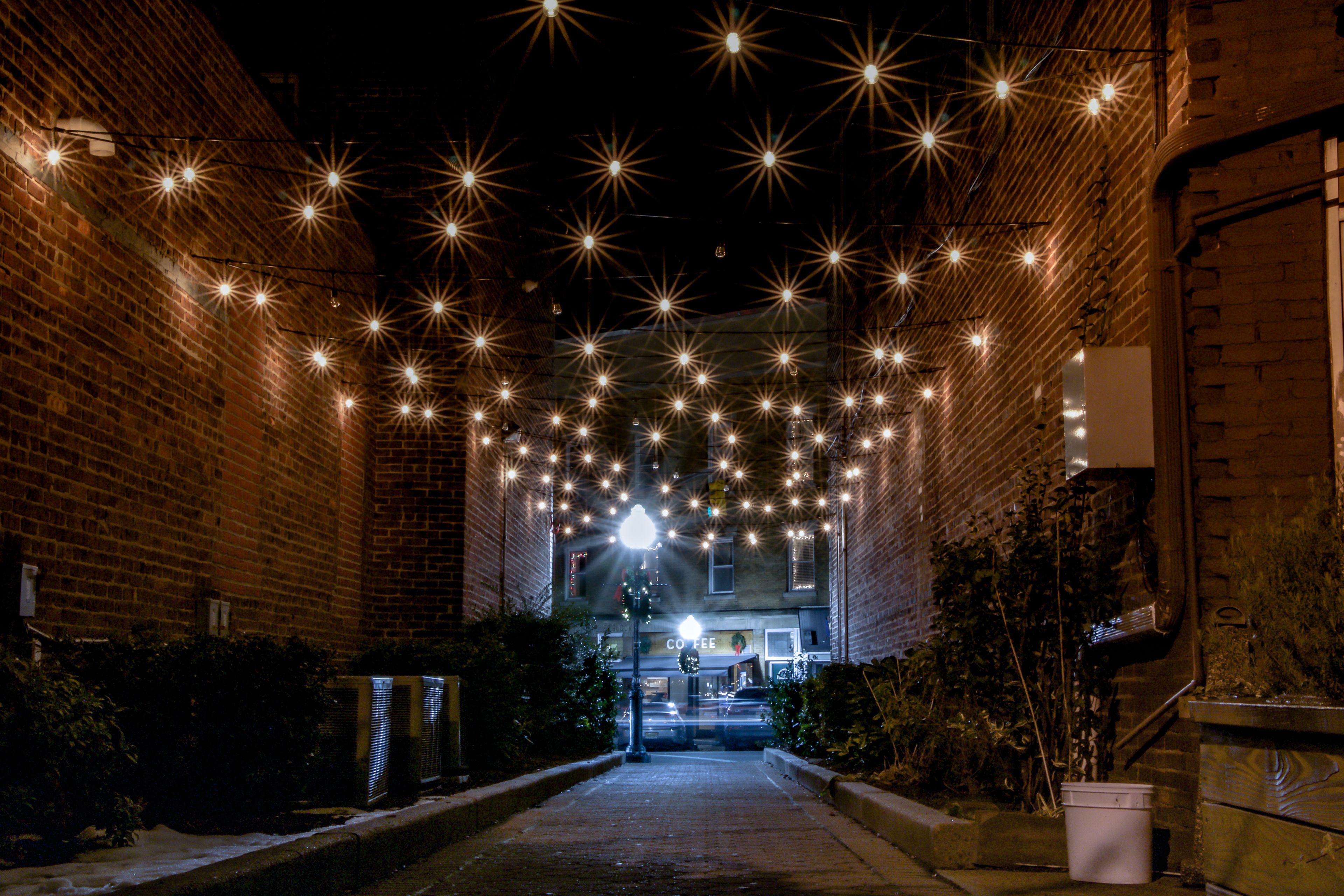 A narrow alleyway with brick walls on either side, adorned with string lights creating a starry effect.