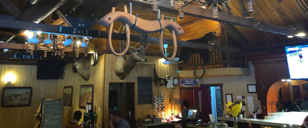 A rustic interior with wooden beams, a chandelier, and a menu board.