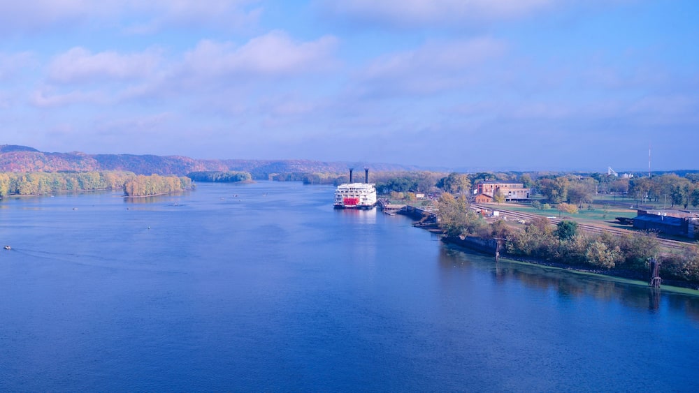 A river with a red boat, surrounded by autumn-colored trees and hills in the background.