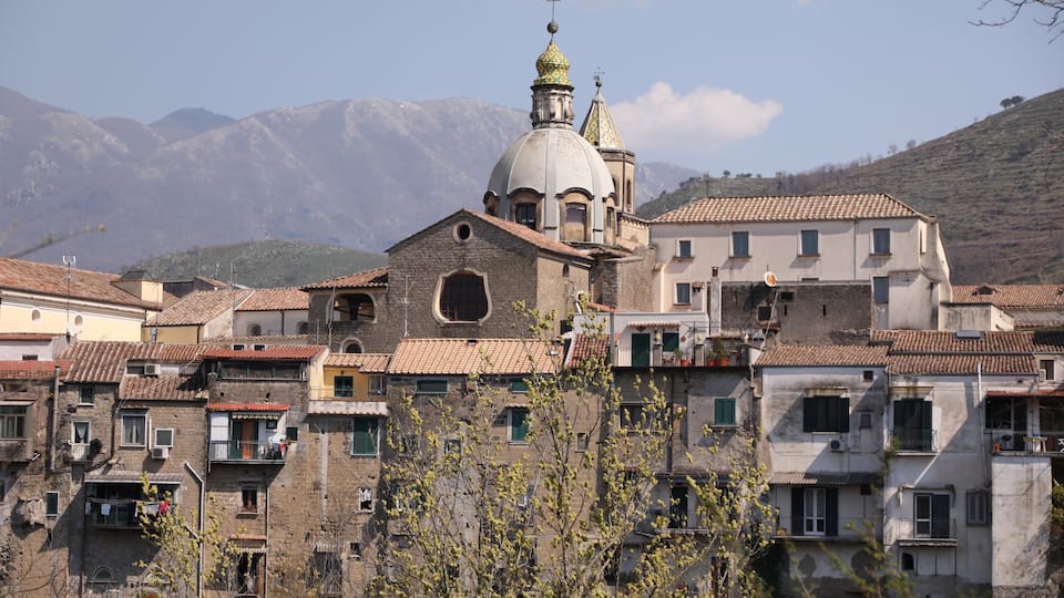 A historic town with a prominent church featuring a golden dome, surrounded by traditional buildings and mountains in the background.