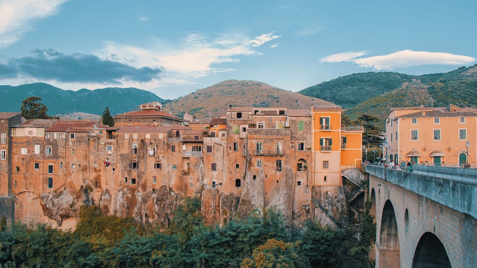 A historic town with old buildings, a bridge, and mountains in the background.