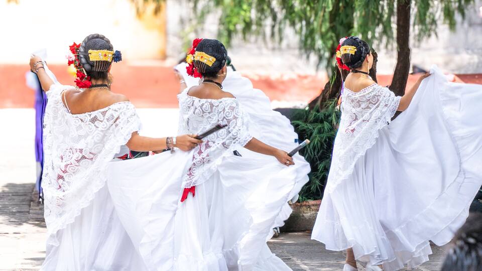 A group of women in white dresses with lace details, dancing outdoors.