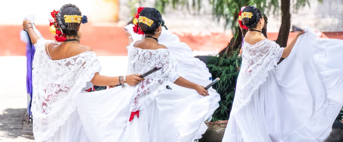 A group of women in white dresses with lace details, dancing outdoors.