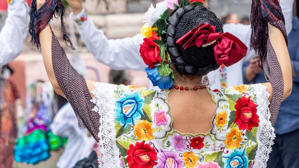 A person with a colorful embroidered blouse and a floral headpiece.