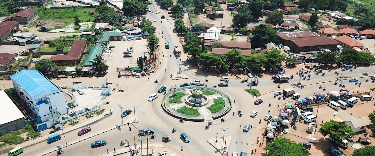 An aerial view of a roundabout surrounded by buildings, vehicles, and greenery.