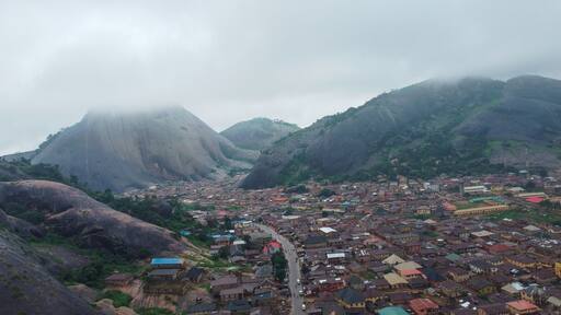 Aerial view of a town nestled between colossal, smooth rock formations under a blanket of clouds, Akure, Ondo, Nigeria.