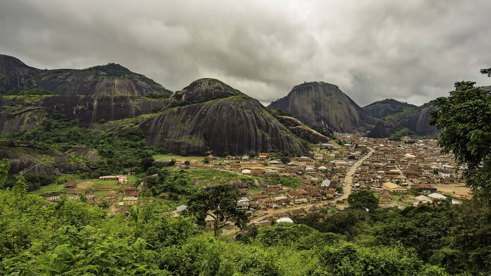 A town nestled between mountains with lush greenery and a cloudy sky.