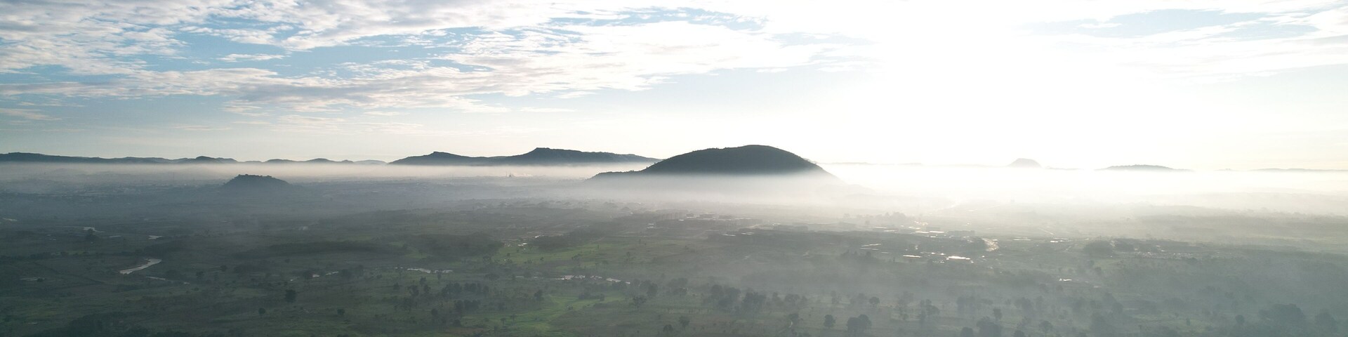 A misty landscape with rolling hills and scattered trees.