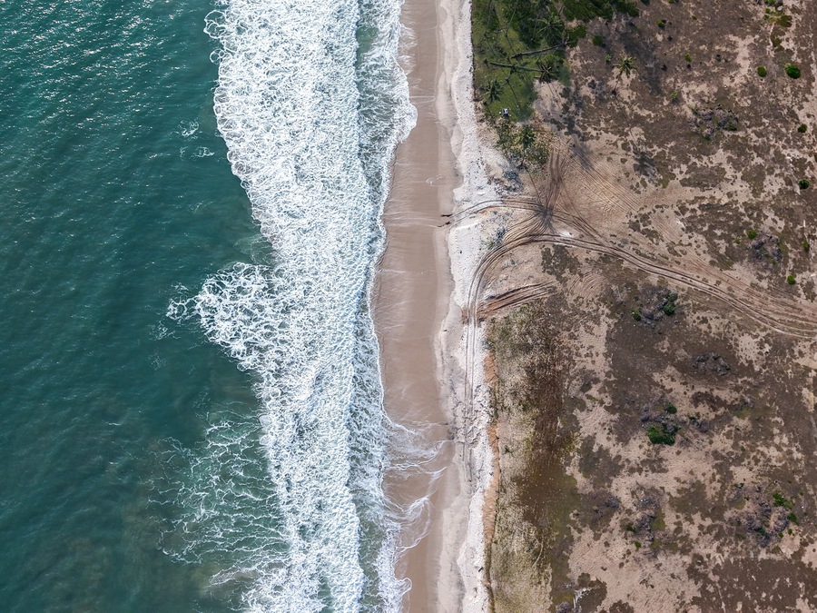 Aerial view of turquoise waves crashing onto the sandy shore contrasting with the earthy tones of the adjacent landscape, Lekki, Lagos, Nigeria.
