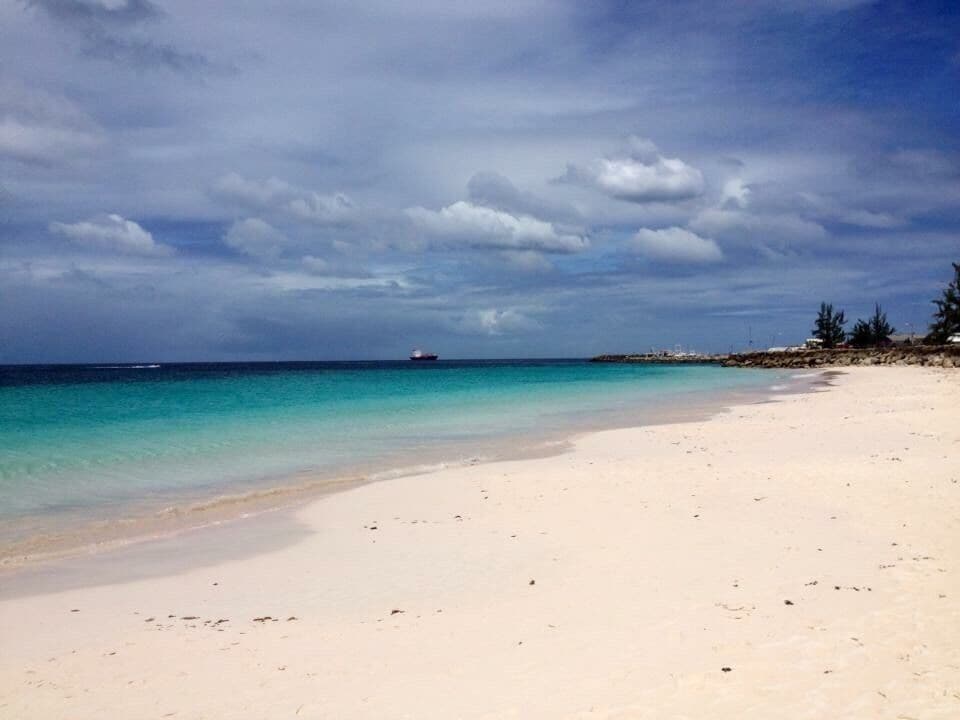 Uma praia com águas azul-turquesa cristalinas, uma costa arenosa e um navio ao longe.