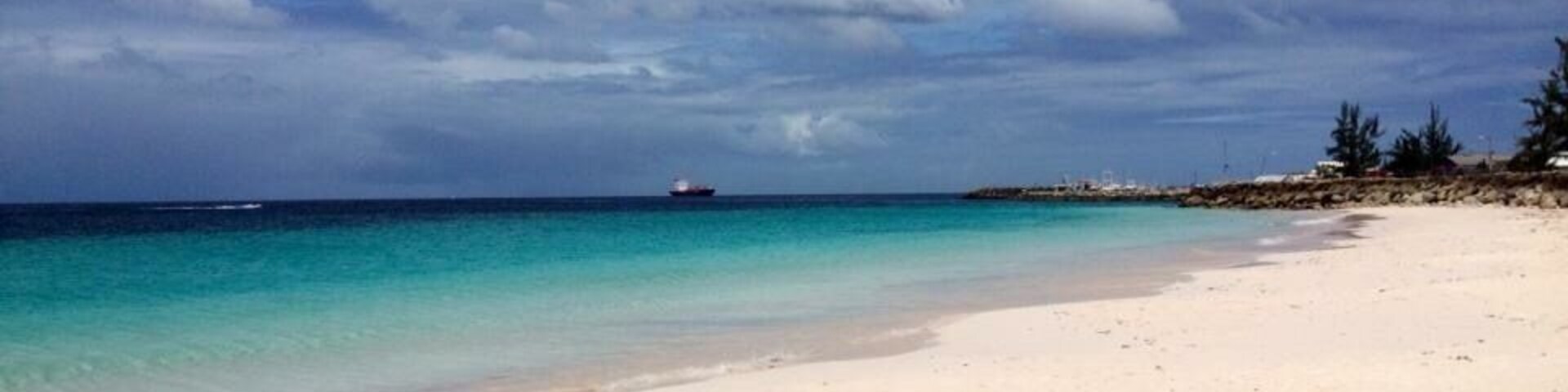 Uma praia com águas azul-turquesa cristalinas, uma costa arenosa e um navio ao longe.