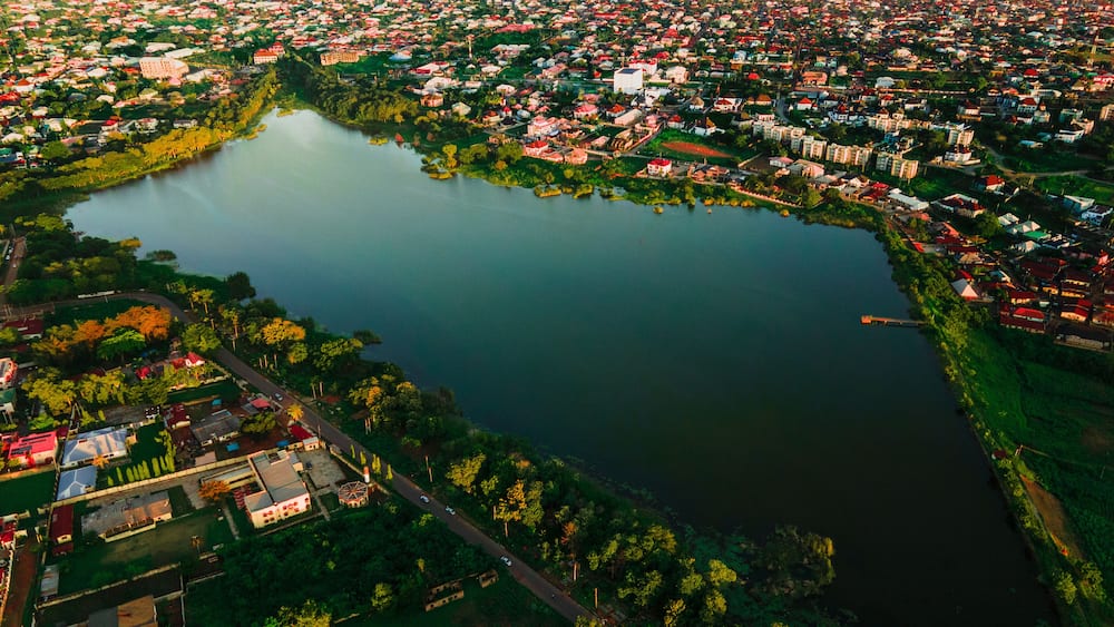 Aerial view of the serene lake reflects the sky, bordered by lush greenery and vibrant buildings, creating a peaceful contrast, Ilorin, Kwara, Nigeria.