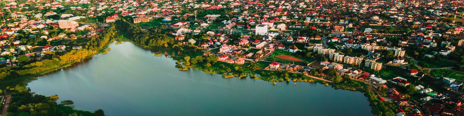 Aerial view of the serene lake reflects the sky, bordered by lush greenery and vibrant buildings, creating a peaceful contrast, Ilorin, Kwara, Nigeria.