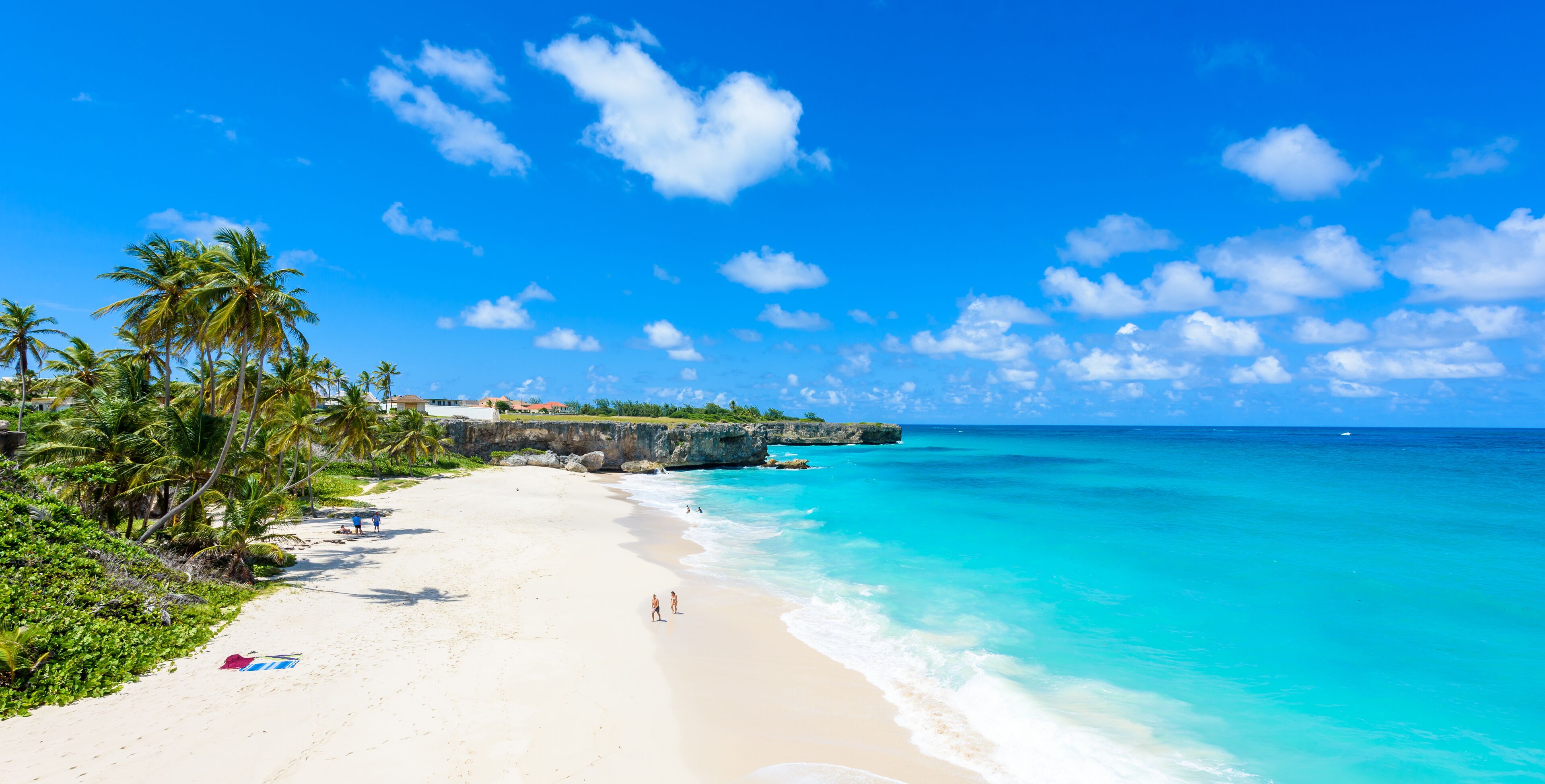 A beach with clear turquoise water, palm trees, and a rocky outcrop in the distance.