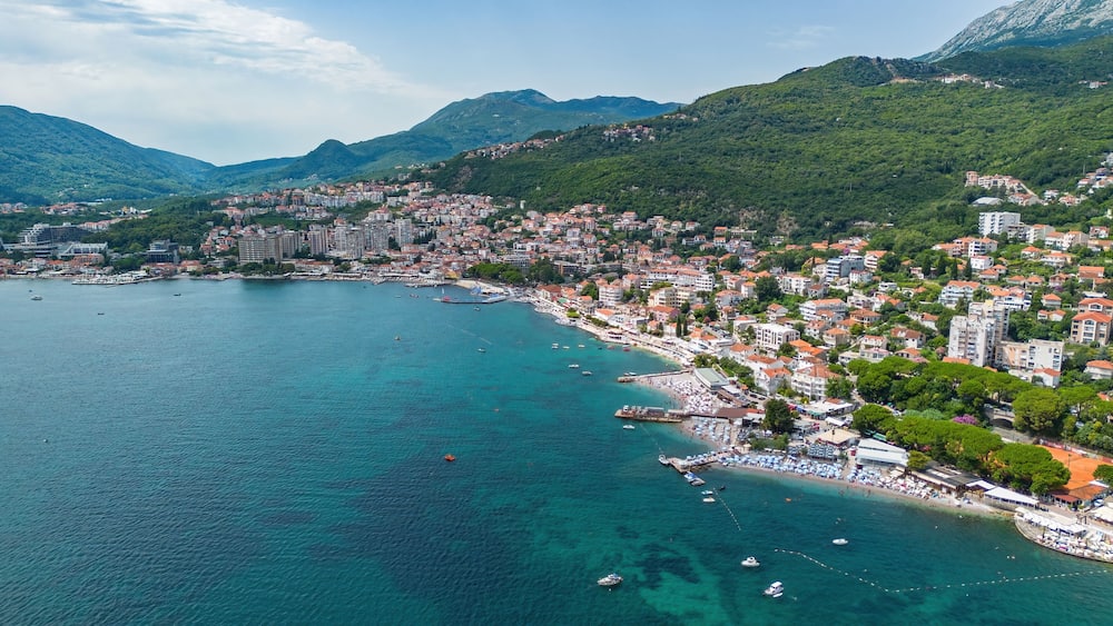 A coastal city with a bay, buildings, and mountains in the background.