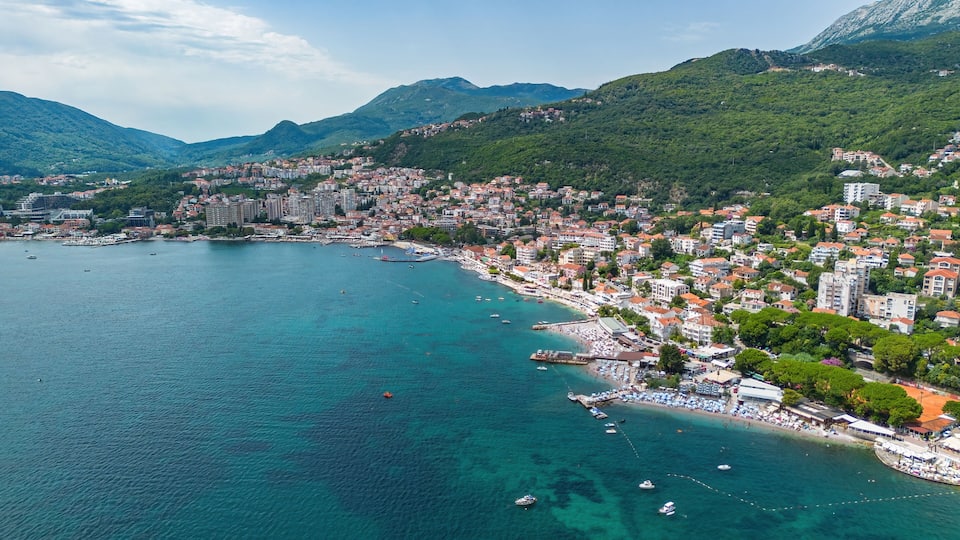 A coastal city with a bay, buildings, and mountains in the background.