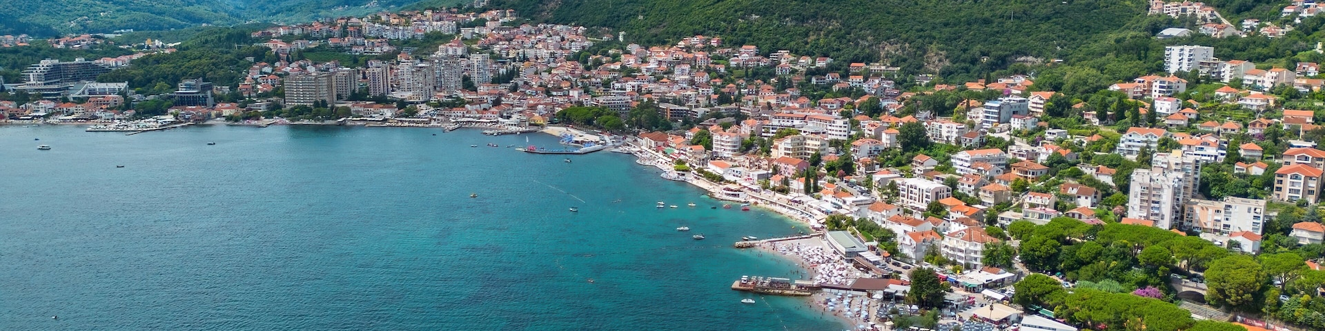A coastal city with a bay, buildings, and mountains in the background.