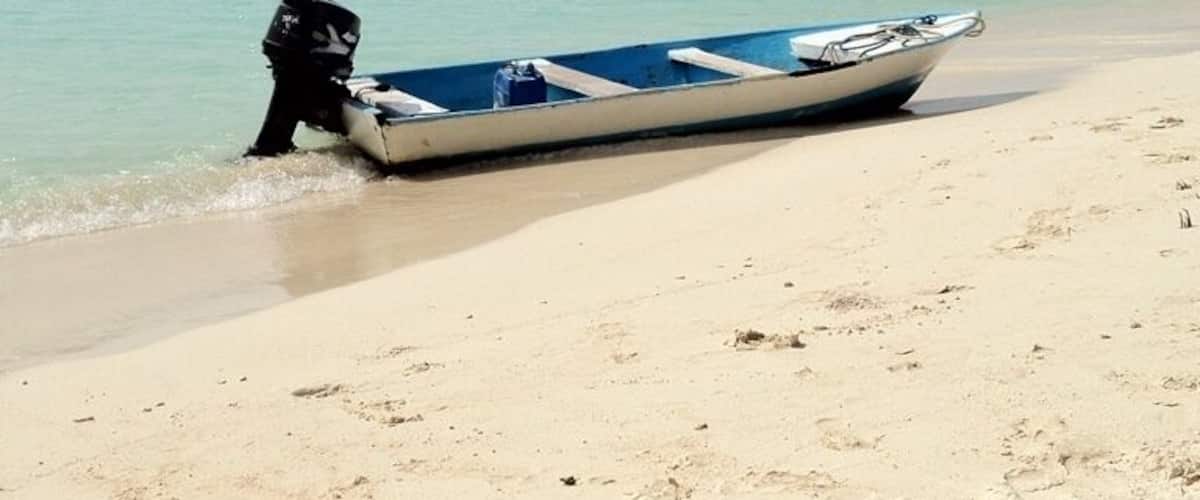 A small boat on a sandy beach with calm water and a distant shoreline.