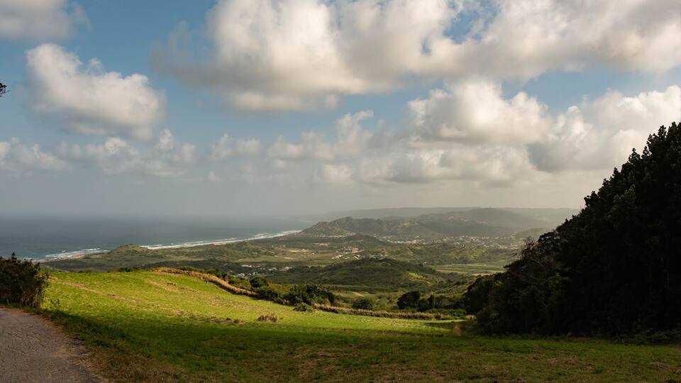 A coastal landscape with rolling hills, a dirt path, and a view of the ocean.