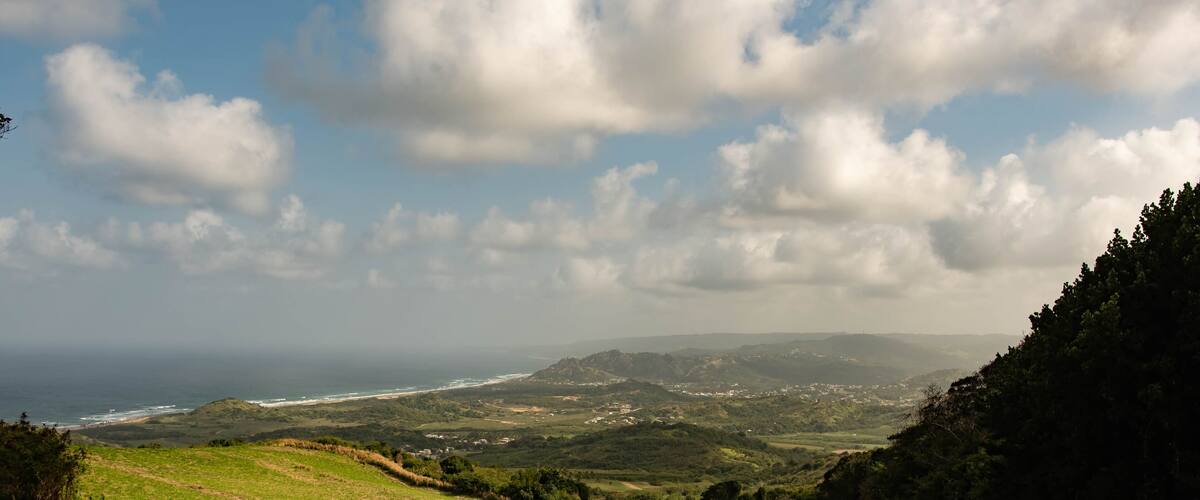 A coastal landscape with rolling hills, a dirt path, and a view of the ocean.