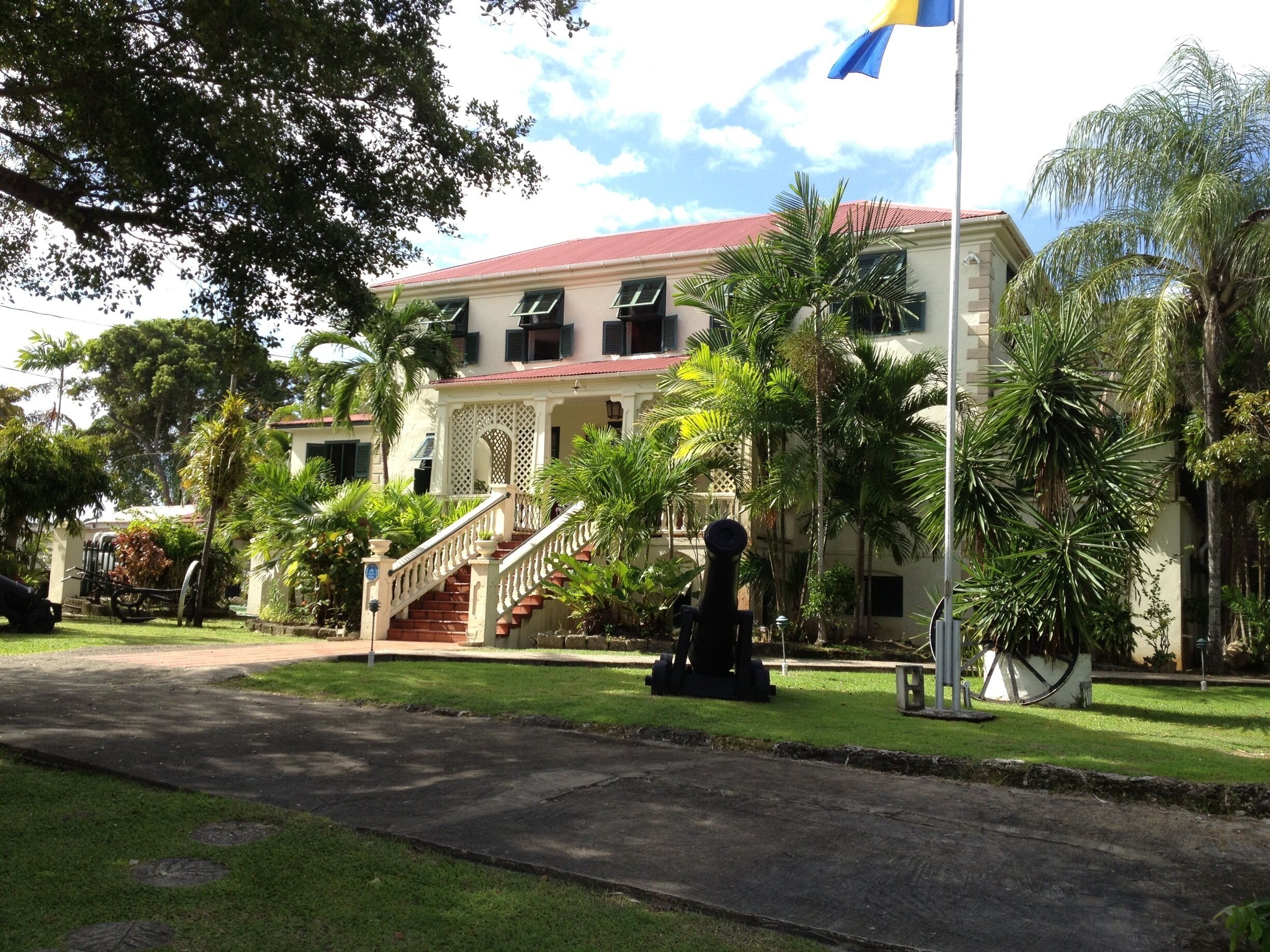 A colonial-style building with a red roof, a staircase, and palm trees.