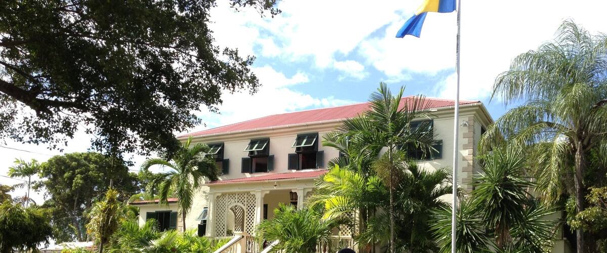 A colonial-style building with a red roof, a staircase, and palm trees.
