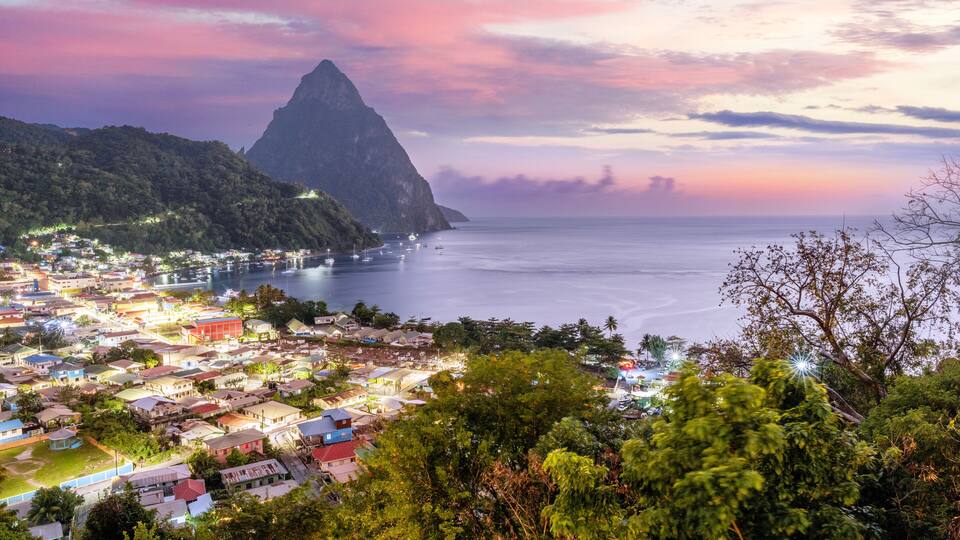 A coastal town with a prominent mountain and a sunset over the ocean.