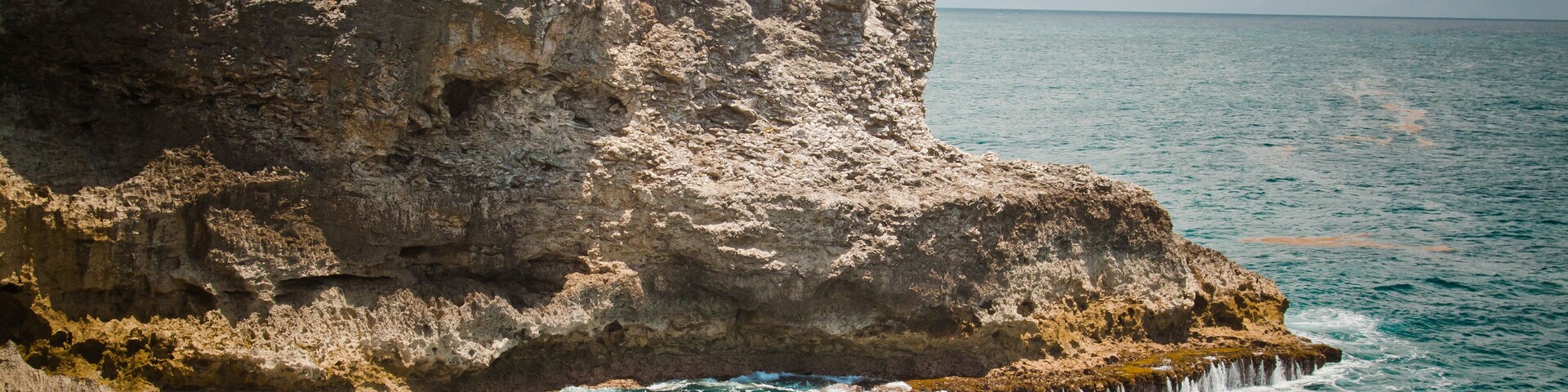 Costa rochosa com uma pessoa em um penhasco, observando águas azul-turquesa.