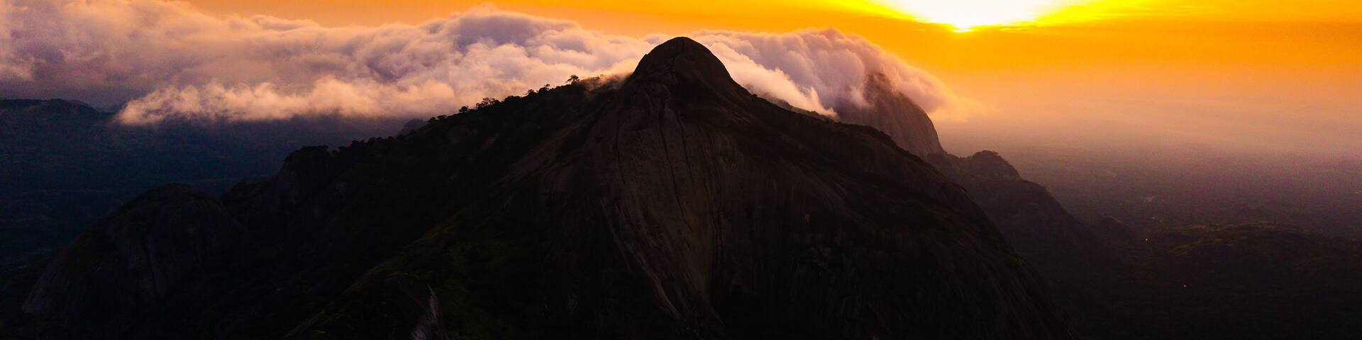 Aerial view of rocky outcrops rise majestically against a fiery sunset, their peaks kissing the clouds in a dance of light and shadow, Idanre, Ondo, Nigeria.