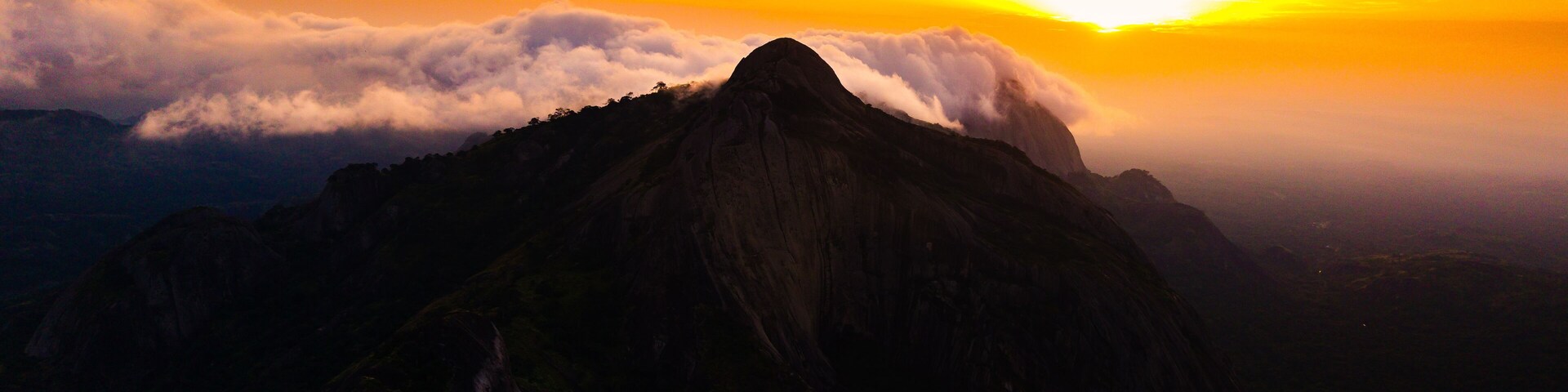 Aerial view of rocky outcrops rise majestically against a fiery sunset, their peaks kissing the clouds in a dance of light and shadow, Idanre, Ondo, Nigeria.