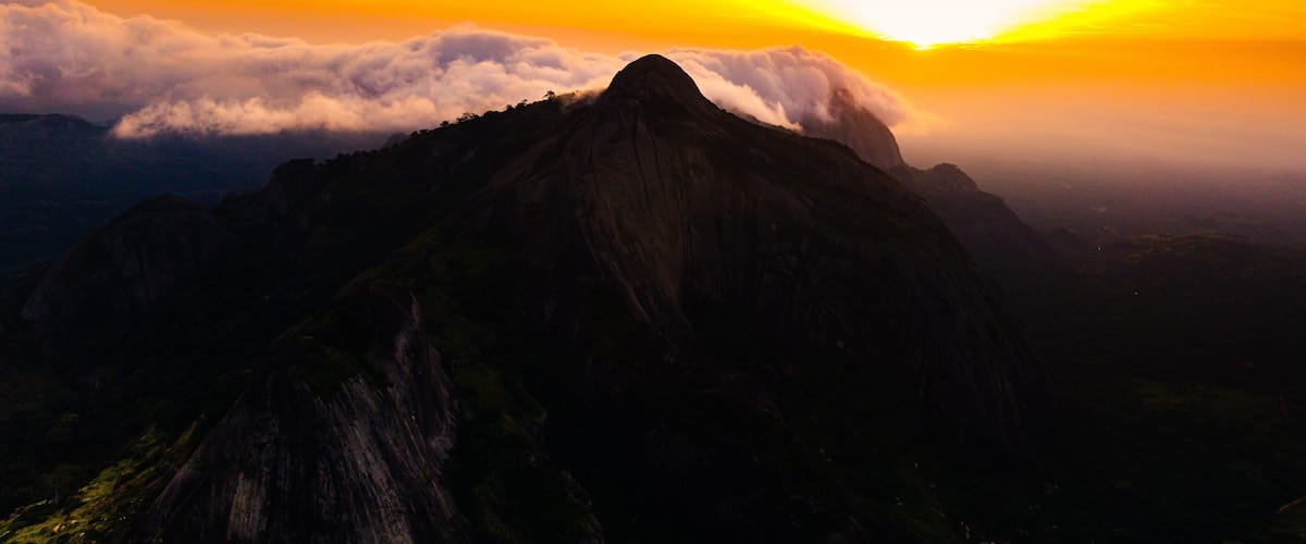 A mountain peak with clouds at its base during sunset.