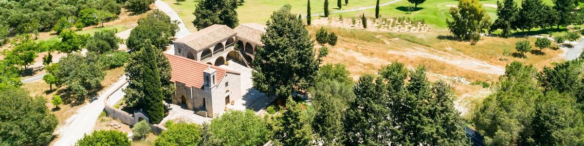 Aerial bird’s eye view of Stavros tis Minthis St Anthony monastery and golf course in Tsada village, Paphos, Cyprus from above. Church surrounded by putting green field, lakes and vineyards in valley.