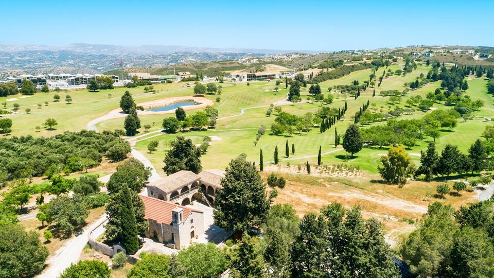 A golf course with a stone building and a view of distant hills.