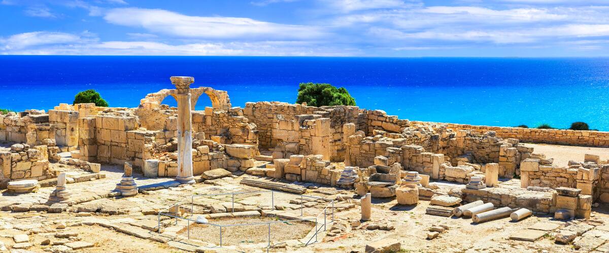 Ancient ruins with columns and stone structures by the sea.