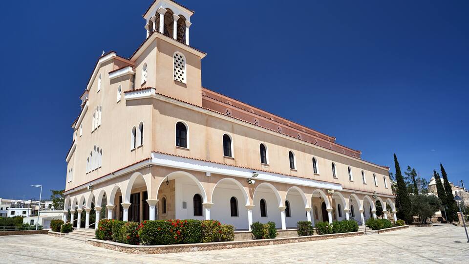 A large building with a bell tower, arched walkways, and red-tiled roof.