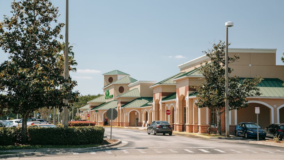 A commercial area with a shopping center, cars parked along the street, and a clear sky.