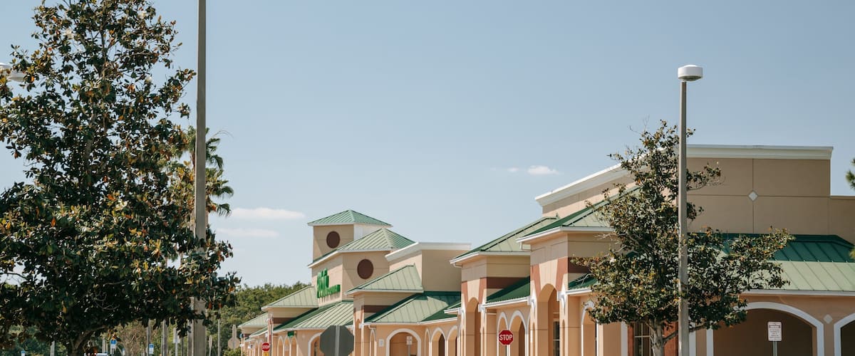 A commercial area with a shopping center, cars parked along the street, and a clear sky.