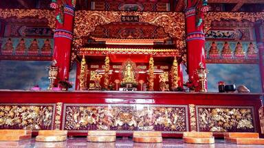 Interior ricamente decorado de um templo, com estátuas douradas, pilares vermelhos e intrincados desenhos florais.