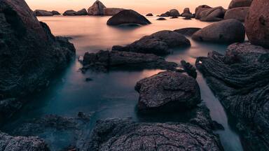 Un paisaje costero con grandes rocas y agua tranquila al atardecer.