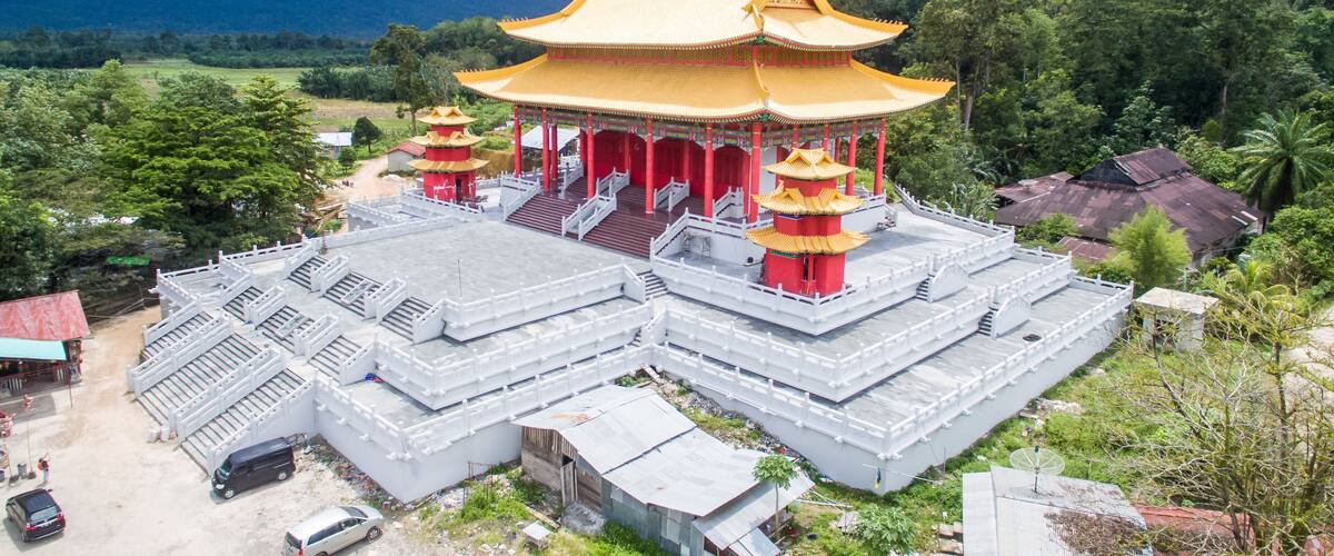 A traditional temple complex with a large central building and multiple smaller structures, surrounded by lush greenery and mountains.