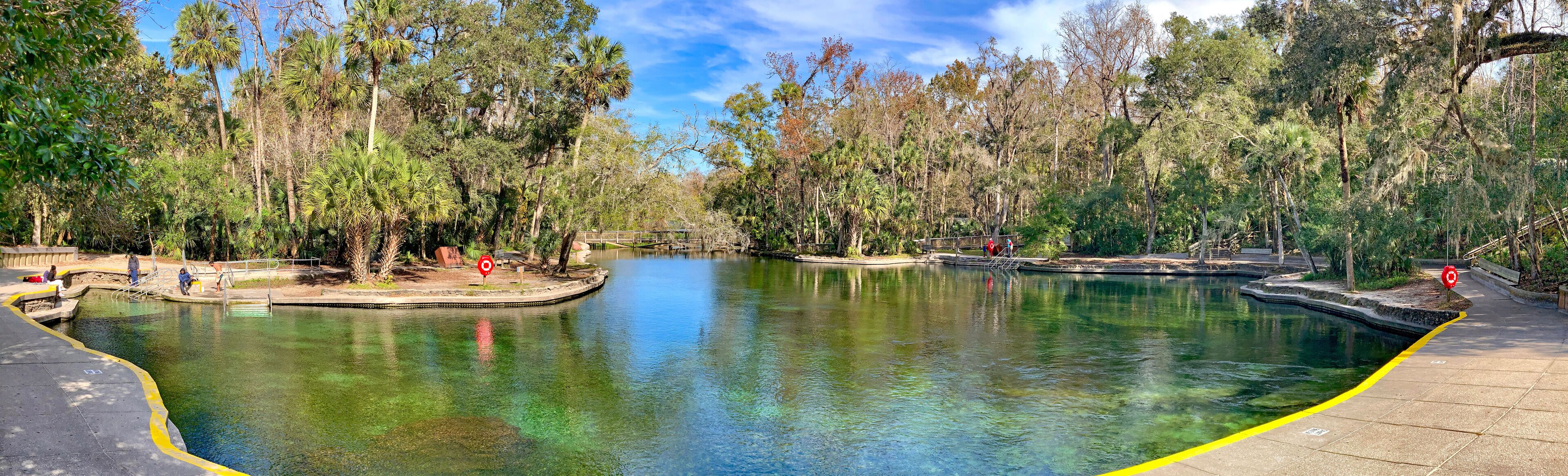 A clear pond surrounded by trees and a walking path.