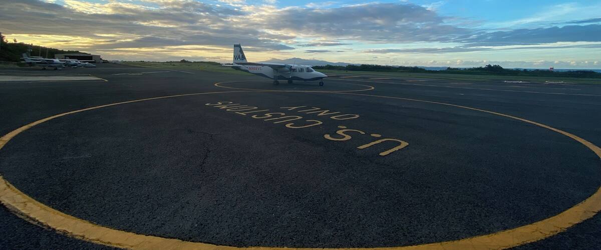 An airport runway with a small aircraft parked on it, under a partly cloudy sky.