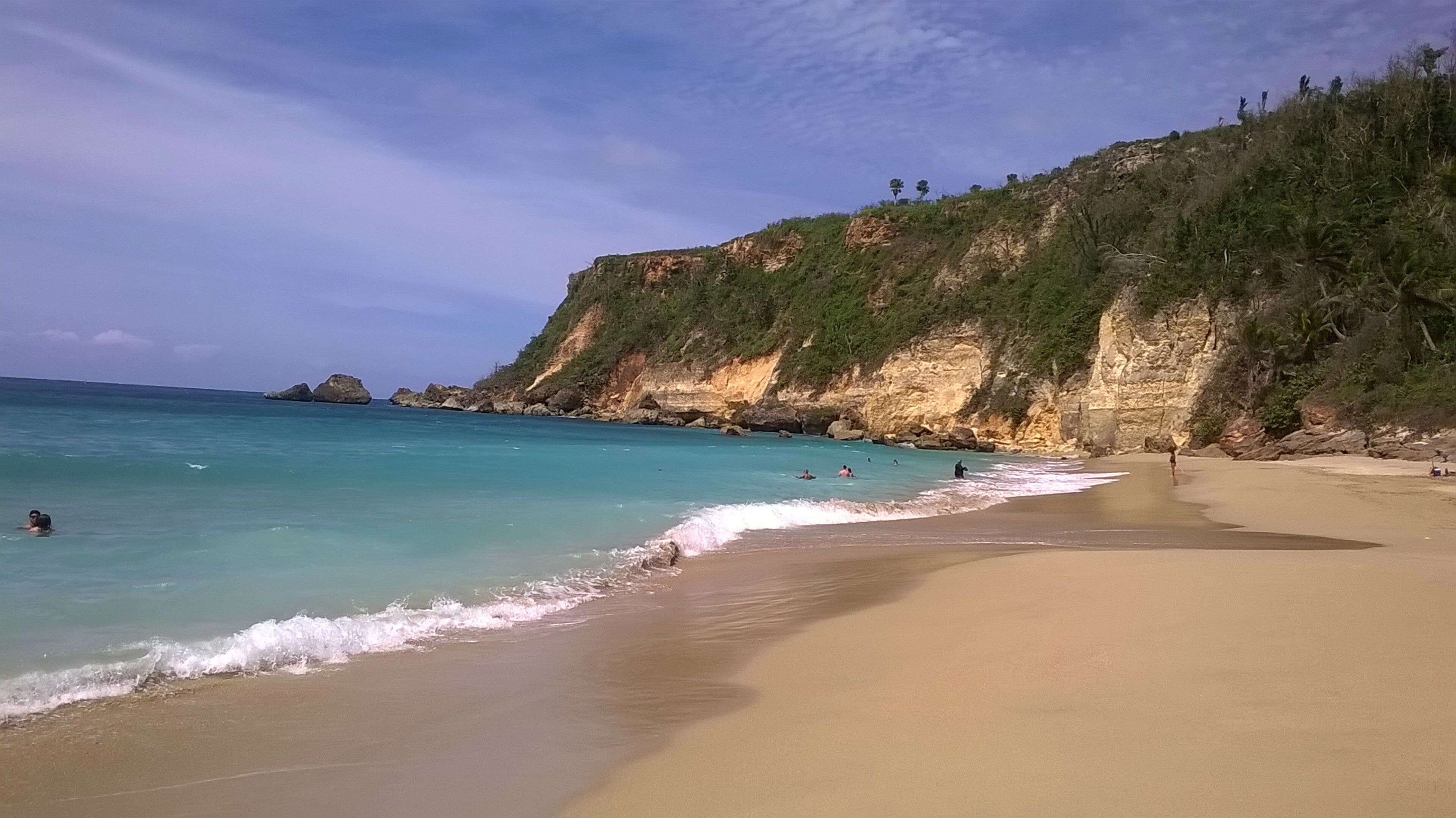 A beach with clear turquoise water, a sandy shore, and rocky cliffs with sparse vegetation.