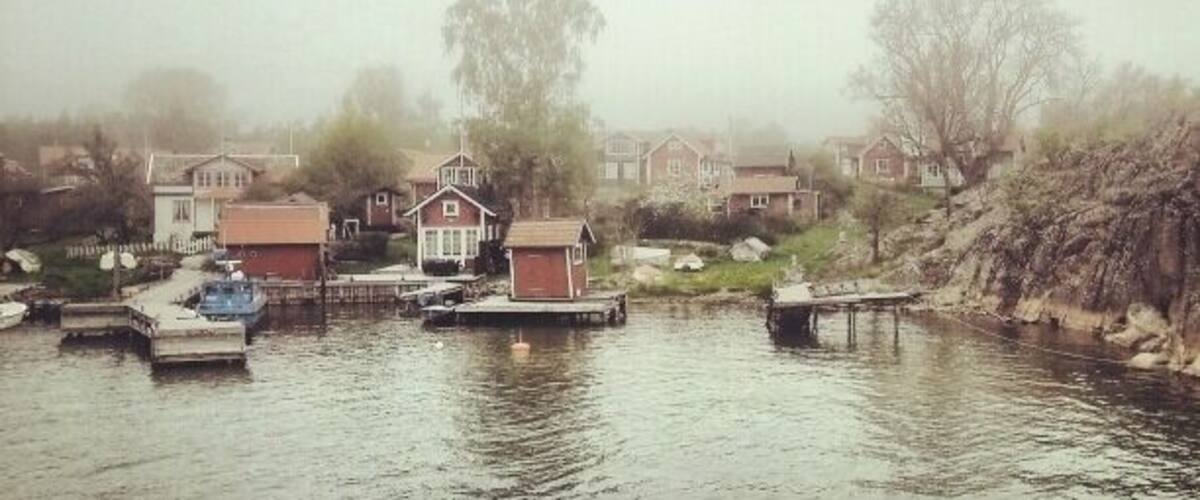 A foggy river with houses and boats.