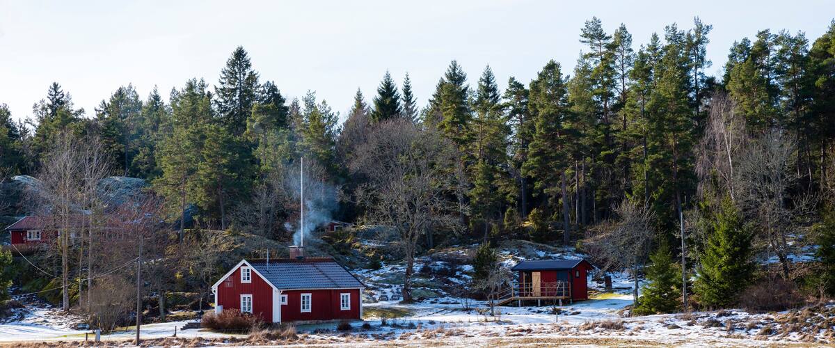 A rural landscape with a red barn, a wooden cabin, and a forested area with snow patches.