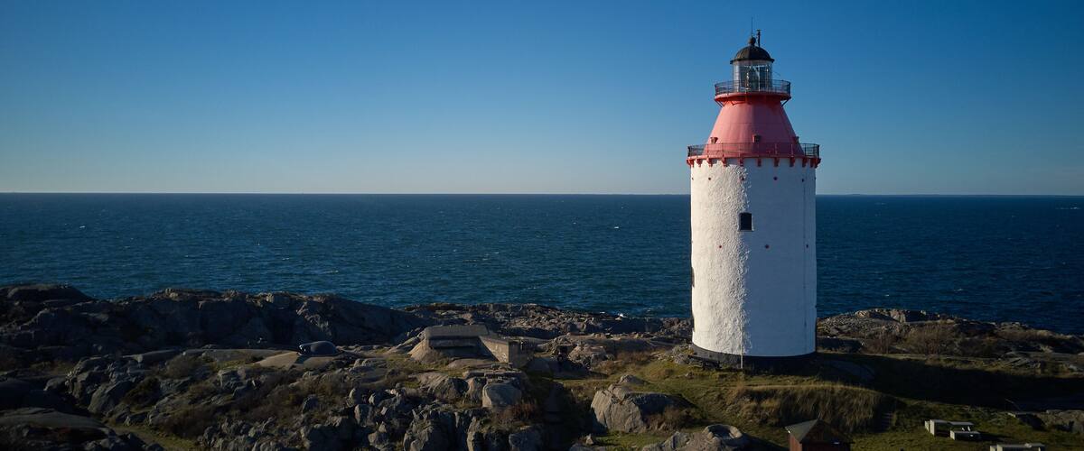 A lighthouse with a red top and white body, situated on rocky terrain near a body of water.