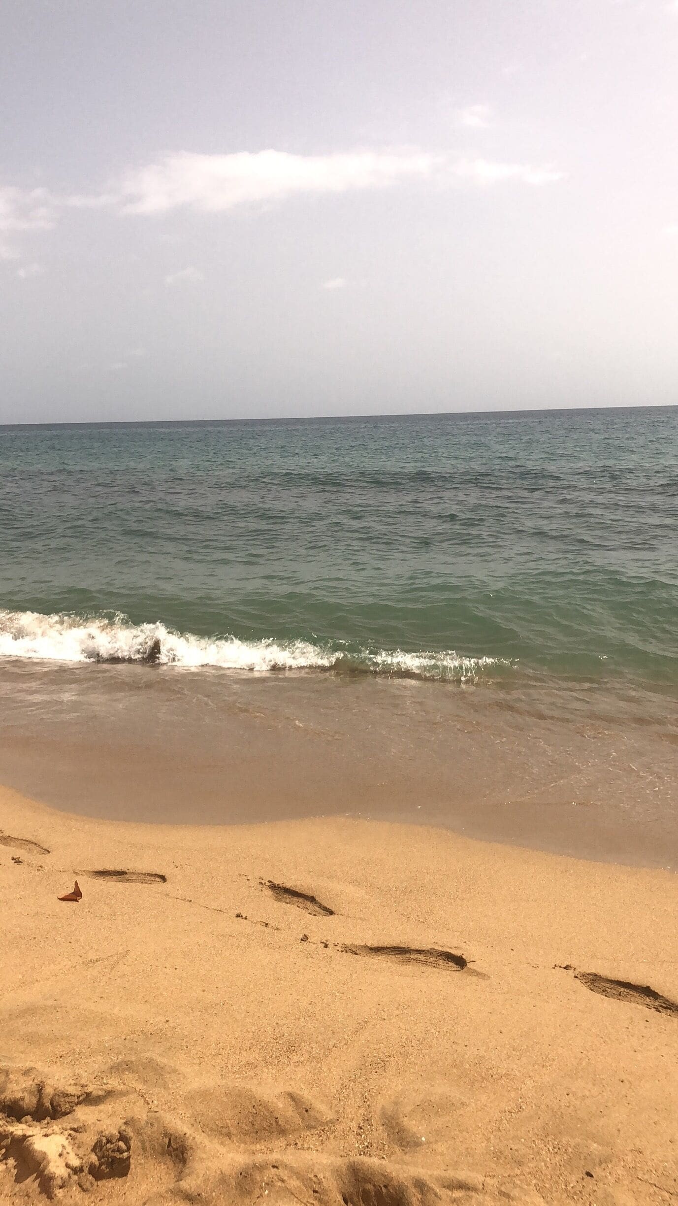A sandy beach with gentle waves and footprints in the sand.